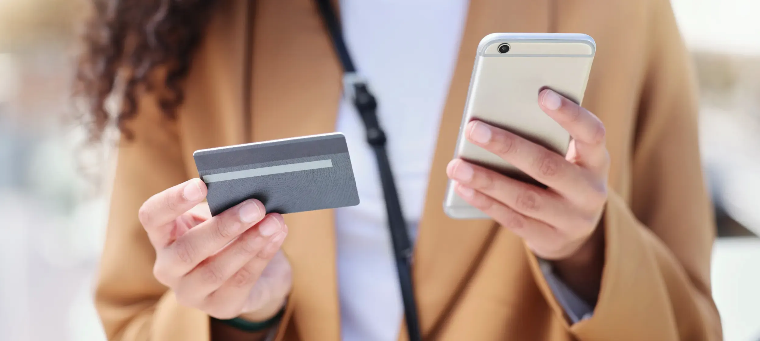 A customer holding a bank card in one hand and a phone in the other