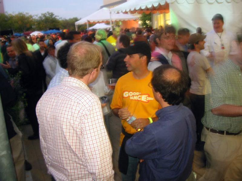 GoogleDance2005.jpg A large crowd of mostly young men mingle in and around marquis tents set up for the Google Dance in 2005. In the center, a man wearing a baseball cap and a t-shirt with the event logo talks to 3 other men.